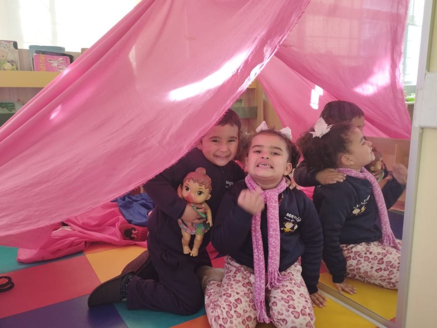 Duas crianças se divertem na cabana feita de lençol na sala do Sesquinho Bagé